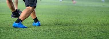 Futbol oyuncuları oyun sırasında dinamik hareket ve enerjiyle bacaklarına ve mavi kramponlara odaklanıyor.