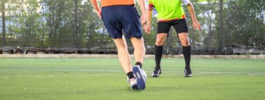 Bir futbol oyuncusu çimen sahası üzerinde hareket halinde, bacaklarına ve toplarına odaklanıyor, açık hava spor ortamında hareket ve rekabet gösteriyor