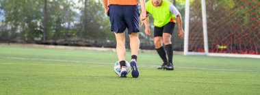 Futbol oyuncuları çim sahada maç yaparken bacaklarına ve toplarına odaklanıyor. Güneşli bir günde spor kıyafetlerini ve spor hareketlerini gösteriyorlar.