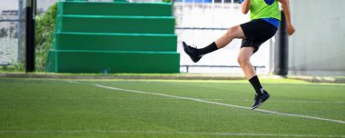 Yeşil tribünler ve arka planda kale direğiyle antrenman sırasında yeşil yapay çim sahasında topa vuran bir futbolcu eylem ve hareketi gösteriyor.