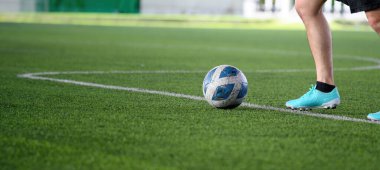 Yeşil çimen sahasında futbol topu. Mavi krampon takan oyuncu maç sırasında tekme atmaya hazırlanıyor. Spor sahasında bacaklara ve topa odaklanıyor.