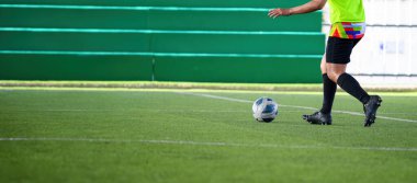 Siyah kramponlu ve renkli şortlu bir futbolcu oyun sırasında yeşil çimlerde topu kontrol ediyor ve spor hareketlerinde odak ve hareket gösteriyor