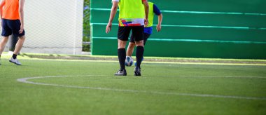 Çim sahası üzerinde oyun sırasında hareket eden bir futbolcu bacaklarına ve toplarına odaklanıyor, spor ortamında hareket ve takım çalışması gösteriyor