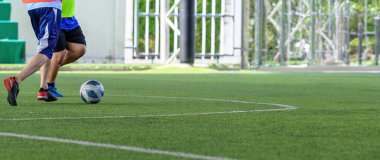 Yeşil çimlerin üzerinde hareket eden bir futbolcu maç sırasında açık hava arka planı ve spor kıyafetleriyle bacaklarına ve toplarına odaklanıyor.