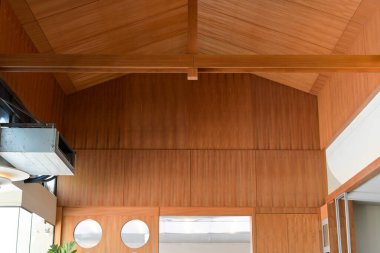 Ahşap kasalı tavana monte edilmiş modern Hvac kanal sisteminin yakın görüntüsü. Doğal ışık ve ahşap panel duvarları olan parlak iç uzayda kirişler var.