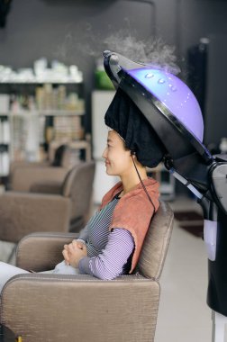 Güneydoğu Asyalı genç bir bayan müşteri boyalı kuaför salonu alıyor. Sağlık hizmetleri rahatlama barışı sunuyor. Genç kız, değerli olarak sunulan saç tedavi sürecinden zevk alıyor