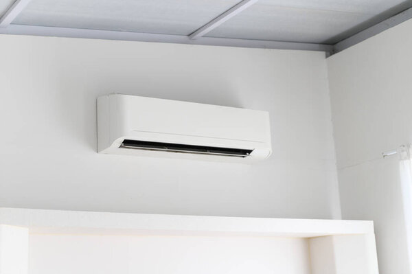 A white air conditioner mounted on plain white wall inside bright room. appliance provides cool air for comfort during hot temperatures. creates relaxing environment in home or office interior