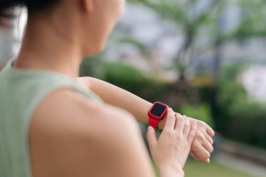 30 'lu yaşlardaki Asyalı kadın nabzı kontrol ediyor. Sağlık hizmetleri için beden eğitimi egzersizi. Şehir merkezinde günbatımında teknoloji kol saati kullanarak sağlıklı bir yaşam tarzı.