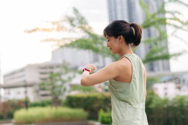 30 'lu yaşlarda odaklanmış Asyalı bir kadın nabız ölçer kalp atış hızını kontrol eder spor yaptıktan sonra akıllı kol saati takılır. Şehir merkezinde gün batımında sağlıklı yaşam tarzı sağlık teknolojisi