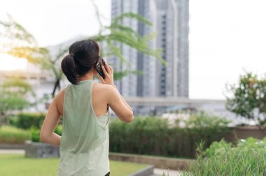 30 'lu yaşlarda odaklanmış Asyalı bir kadın akıllı telefondan antrenörden spor tavsiyesi alıyor. Günbatımında şehir parkında teknolojiyle sağlık ve sağlık hizmetleri için sağlıklı bir yaşam tarzı egzersizi