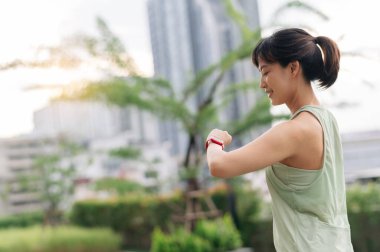 Gülümseyen 30 'lu yaşlardaki Asyalı kadın nabzını kontrol ediyor ve kalp atış hızı spor yaptıktan sonra akıllıca hareket ediyor. Teknolojik kol saati ile sağlıklı bir yaşam tarzı ve sağlık. Sağlık hizmetleri. Şehir günbatımı.