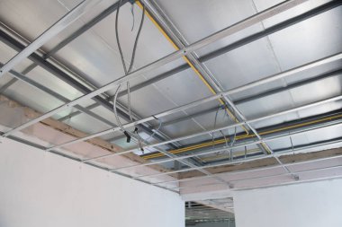 Yeni elektrik kablolarına sahip alüminyum tavan iskeleti, bir iç yenileme projesi sırasında kurulum sürecini gösteriyor. Metal şebeke yapısı tamamlanmamış tavanı destekler