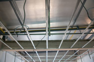 Metal tavan iskeleti içinde elektrik tesisatı kurulumunu gösteren bitmemiş bir iç yenileme projesi. kompleks alüminyum ızgara inşaat çalışmalarının ayrıntılarını gösterir