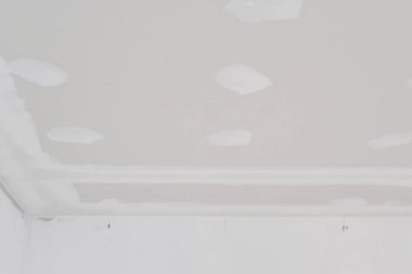 İçerideki binanın içinde elektrik kablosu yerleştirilmiş alçıtaşı tavanı pürüzsüz kenarları ve pürüzsüz bir kaplama oluşturmaya hazır alanları gösteriyor