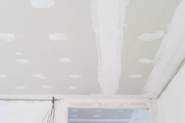 İç bina yenileme projesinde pürüzsüz alçıtaşı tavan kurulumu görülebilir elektrik teli ve pürüzsüz kenarlı eklem sıva son kaplama için hazırlanıyor