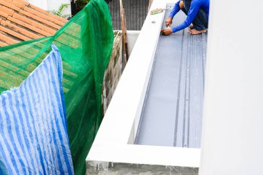 Çalışkan inşaat işçisi yalıtım ve kaplama için pu köpüğü kullanarak kıvrımlı metal çatı paneli kuruyor. El işçiliği çatısı inşaatı, yoğun çalışmayı ve birlikte çalışırken odaklanmayı gösteriyor