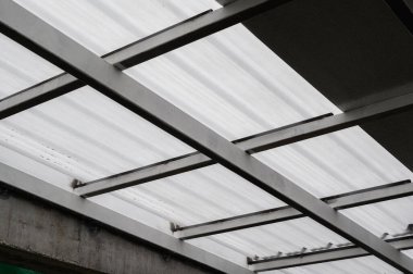 Çatı kaplamasını destekleyen metal kirişler. Işık, kıvrımlı çarşafların arasından filtrelenerek desenler oluşturur. Güçlü metal iskelet, başımızın üstünde istikrar sağlıyor. Dayanıklı sayfa materyali