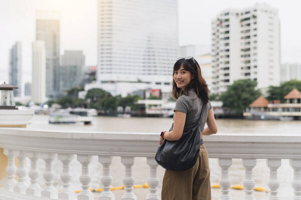 Happy solo southeast asian woman teenager blogger. World travel and asia tourism concept. Local cultural experience for explorer to wait for express boat on Chao Phraya River Bangkok Thailand