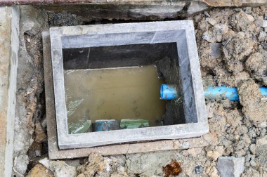 Ev tadilatı sırasında kirli suyla beton boşaltma çukuru açılır. Hasarlı septik sistem ya da su tesisatı mavi PVC boruyla yer altında onarılmayı bekliyor.