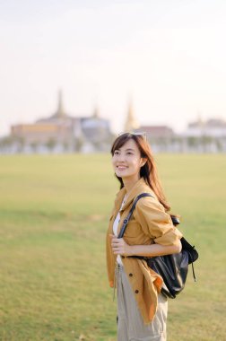 Sırt çantalı Asyalı bir gezgin tapınağın önünde gülümsüyor, açık hava macerasının ve sıcak güneş ışığında kültürel keşiflerin tadını çıkarıyor.