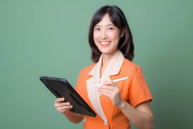 Güneydoğu Asyalı bir kadın internet kullanırken gülümsüyor stilus kalemle, yeşil arka planda duruyor, profesyonel ve kendinden emin ifade