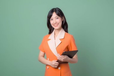 Elinde tablet tutarken gülümseyen Güneydoğu Asyalı bir kadın, yeşil arka plana karşı duruyor, internet teknolojisini ve profesyonel ortamdaki modern iletişimi temsil ediyor.