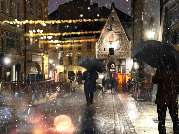 Night city street man with umbrella walk on medieval street house festive garland and first snow with rain in Tallinn old town travel Estonia