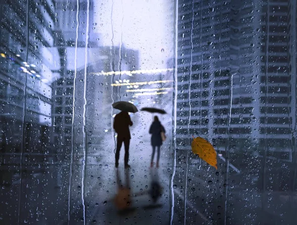Autumn  Rainy drops on window , couple man and woman  with umbrella silhouette reflection Modern buildings facade windows evening blurred light in glass business urban architecture