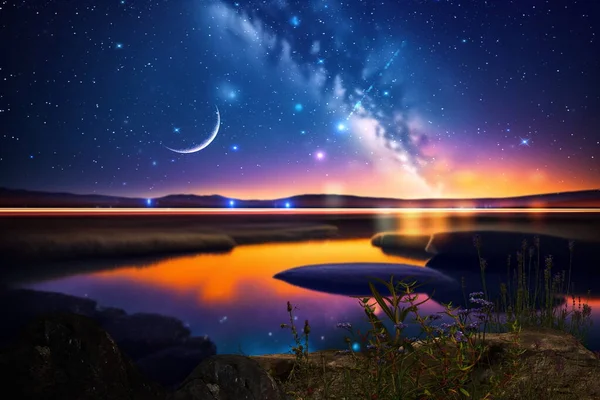night at sea starry sky and moon on dramatic clouds sea water wave and stones on horizon blurred city light