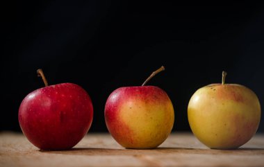 Elmaların önü koyu arkaplan görünümlü ahşap bir masada üç elma.