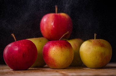 Masanın üzerinde bir demet elma var. Siyah arka planda güzel kırmızı-pembe yeşil elmalar.