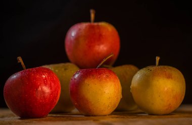 Masanın üzerinde bir demet elma var. Siyah arka planda güzel kırmızı-pembe yeşil elmalar.