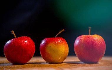 Elmaların önü koyu arkaplan görünümlü ahşap bir masada üç elma.