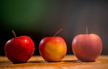Elmaların önü koyu arkaplan görünümlü ahşap bir masada üç elma.