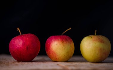 Elmaların önü koyu arkaplan görünümlü ahşap bir masada üç elma.