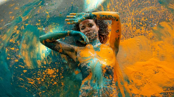 年轻性感的裸体女子上身涂着蓝色 橙色和绿松石色 躺在工作室地板上装饰典雅 创造性地 抽象地表现身体艺术和绘画 复制空间 — 图库照片