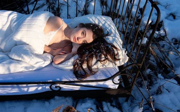 snowy winter landscape of a frozen lake, with attractive, young, sexy, brunette woman, in white underwear, lingerie lying relaxed in bed, copy space
