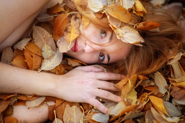 赤とオレンジの秋の葉で覆われた若い美しい赤毛の女性の肖像画を閉じます 美しいセクシーな女の子は秋の葉の上に横たわる 赤い黄金の葉の下の若い女性の顔 コピースペース — ストック写真