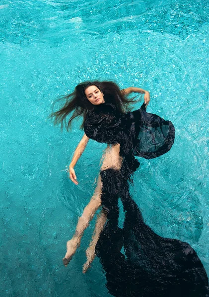 俯瞰一位身穿黑色礼服的年轻貌美的性感女子 毛巾飘浮在碧绿的池水中 轻盈而优雅地游泳 复制空间 — 图库照片