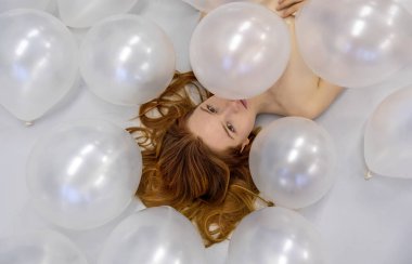 Beyaz yanardöner balonlar arasındaki genç, şehvetli kızıl saçlı kadının moda portresi.