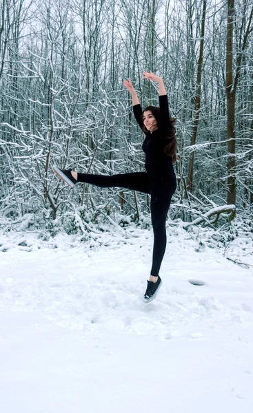 Genç, güzel, esmer kadın balerin kız, siyah bale elbisesi içinde, karlı kış ormanlarında mutlu bir şekilde zıplıyor, boşluğu kopyalıyor.