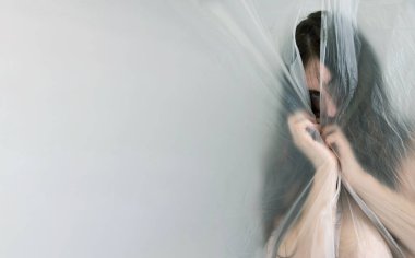 Genç, uzun saçlı bir kadının bulanık, bulanık portresi plastik folyonun arkasındaki izole hayal dünyasından dışarı bakıyor, tek gözüyle, fotokopi uzayı.