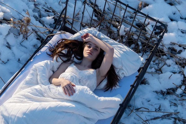 Top view of attractive, young, sexy, brunette woman, in white underwear, lingerie lying relaxed in bed in icy frozen snowy winter, blue shadow, copy space