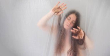 Pankart bulanık, bulanık, erotik romantik kadın portresi plastiğin arkasında, aşağıya bakıyor, saçlarıyla utangaç oynuyor, coşkuyla hareket ediyor, boşluğu kopyalıyor.