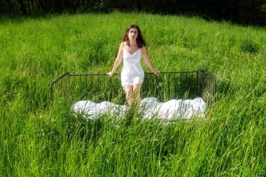 Genç ve seksi bir kadın güneşli bir yaz gecesinde duruyor yemyeşil çayırlar beyaz gecelik içinde, boşluğu kopyalıyor.