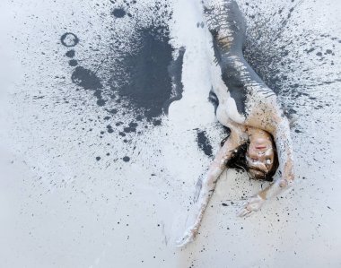 sexy nude woman in black and white color painted, lying decorative on the white, black, gray Studio floor, rolls to the side and leaves an imprint of her body, copy space