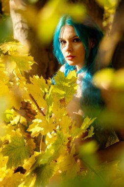 Beautiful sexy young woman with blue hair in yellow golden maple autumn leaves