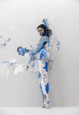 young sexy woman in underwear, lingerie, artistically abstract painted with white and blue paint, with a beautiful round erotic butt stands at the studio wall, copy space