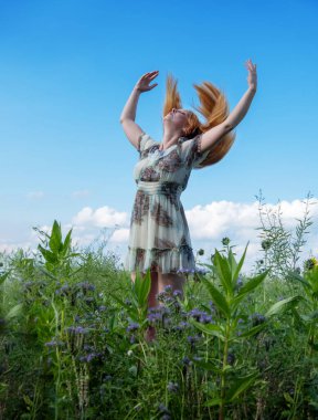 Güzel, genç, seksi kızıl saçlı kadın sahada, kollarını kaldırıyor, evrenin enerjisini elde etmek için kollarını açıyor, uzun kızıl saçlar, neşe, özgürlük, mutluluk, kopyalama alanı.