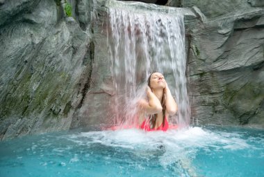 Pembe Bikini 'li genç, güzel, seksi sarışın kadın Spa Sağlık Havuzu' ndaki şelalenin dalgalanan suyunun tadını çıkarıyor. Düşen suyu hissediyor, boşluğu kopyalıyor.